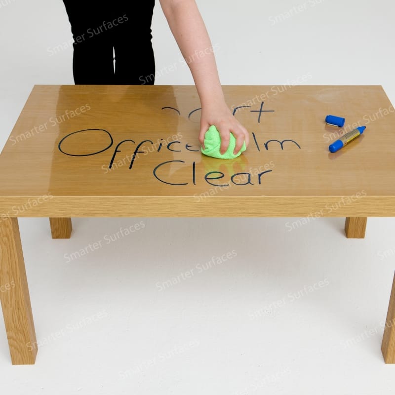 A person writing on a clear self-adhesive whiteboard film applied to a table