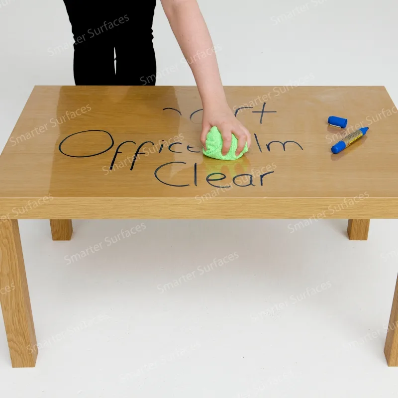 A person writing on a clear self-adhesive whiteboard film applied to a table