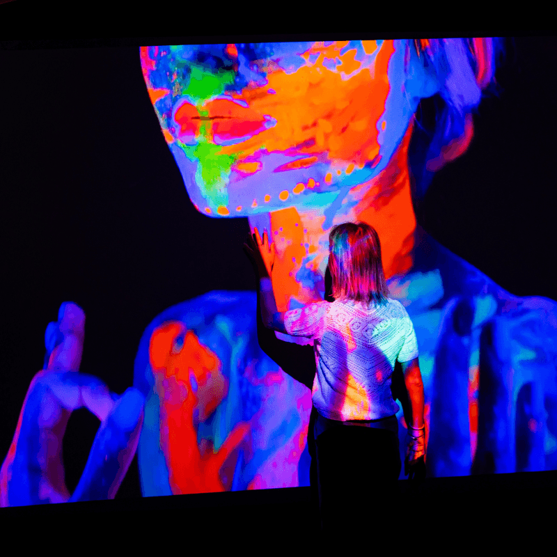 Person interacting with colorful digital art projection on a clear projector screen