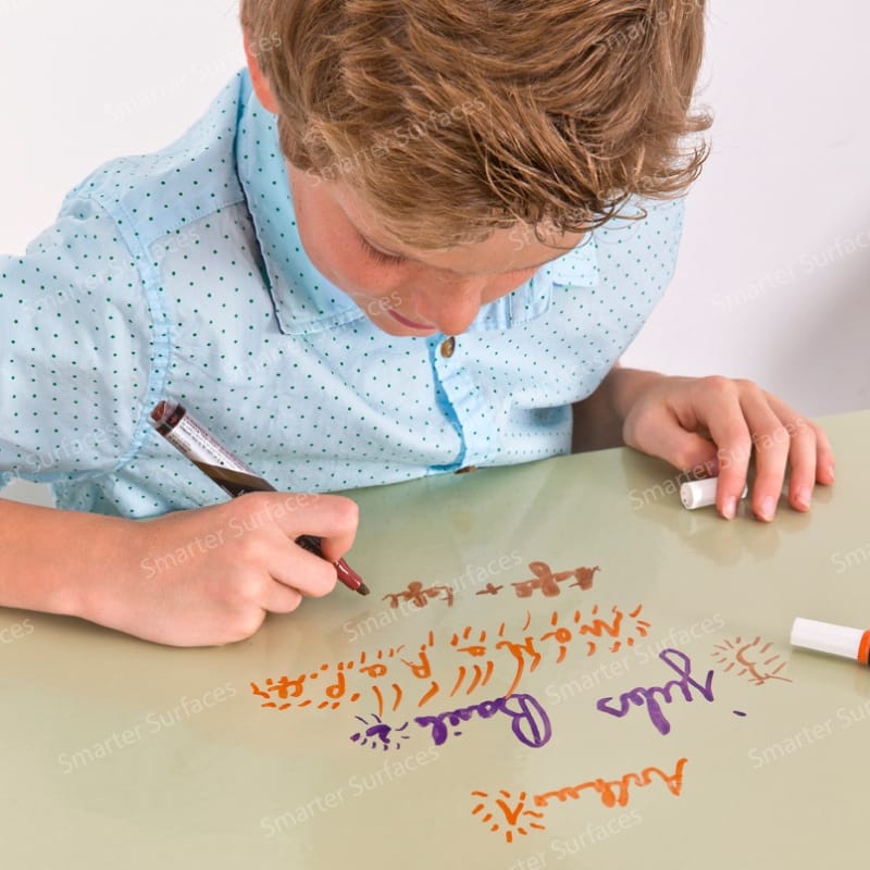 Child writing on a clear dry-erase film placed on a desk