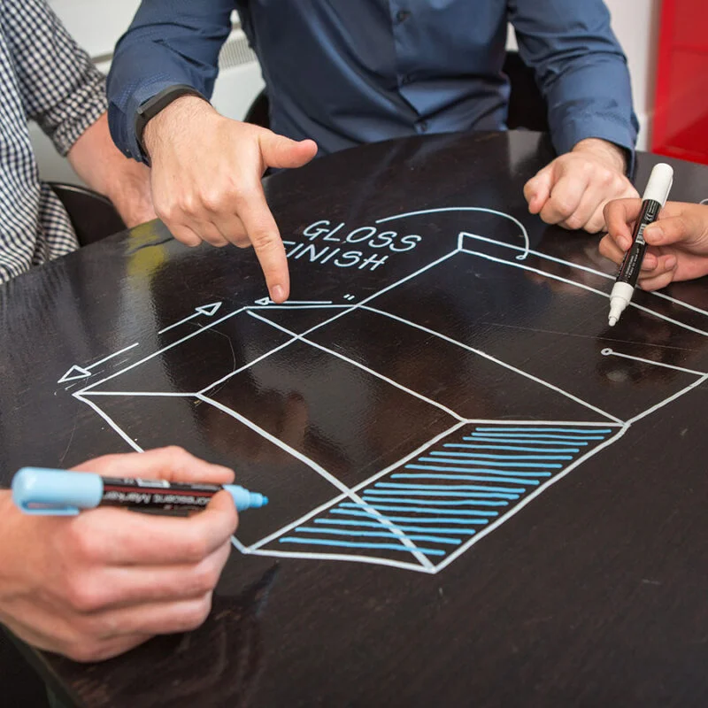 Employees using markers on clear whiteboard paint lunch table