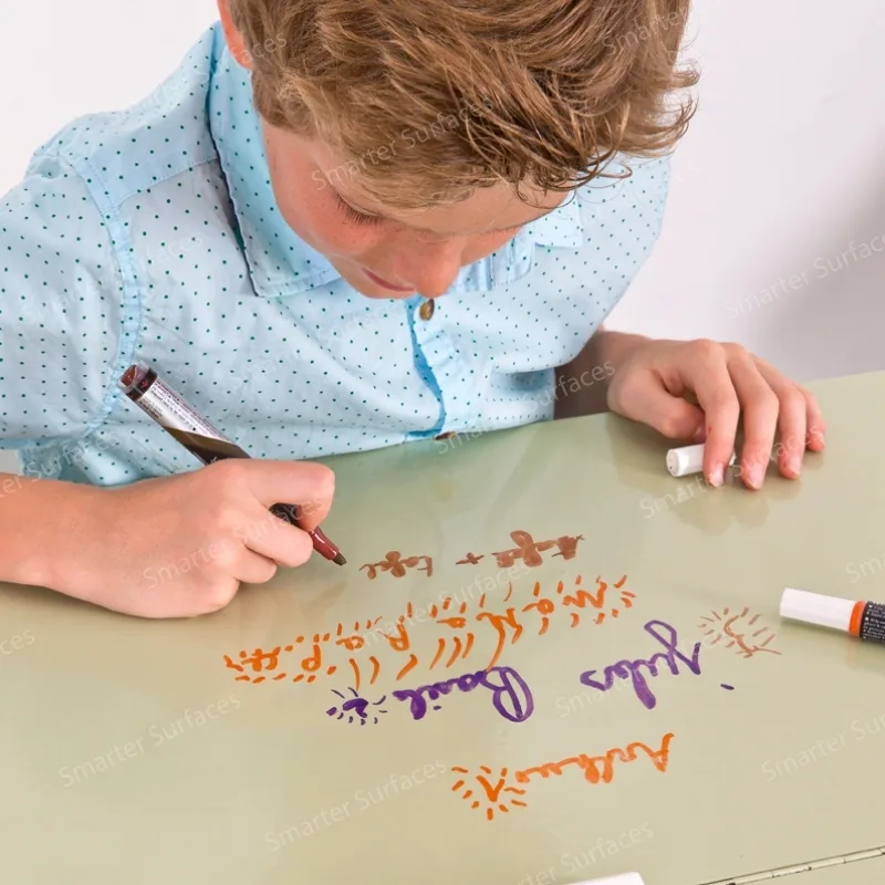 Young boy drawing with markers on a dry erase paint surface