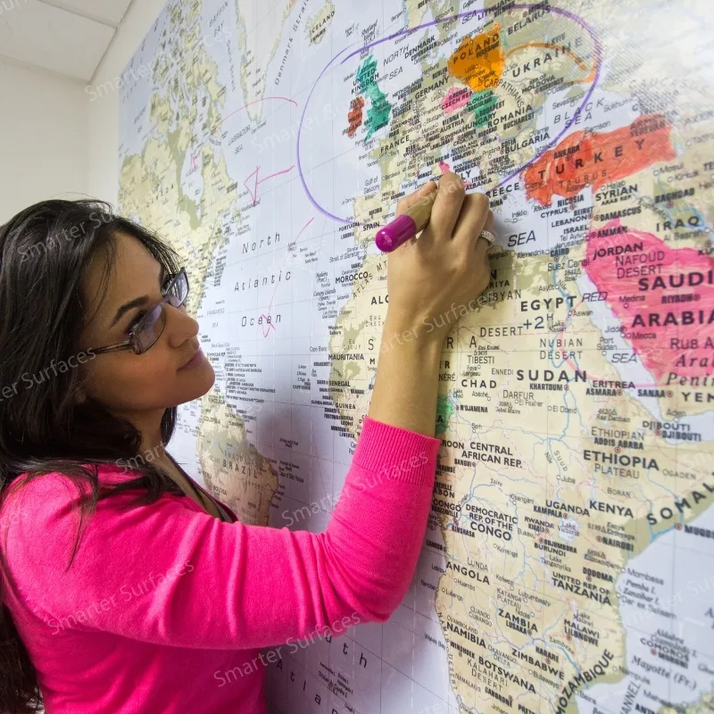 A woman using whiteboard wall paint to draw on a world map with markers