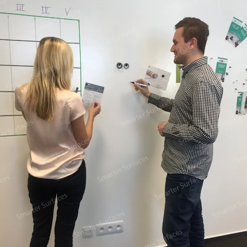 Two professionals collaborating and arranging documents and materials on Black Magnetic Paint Wall.