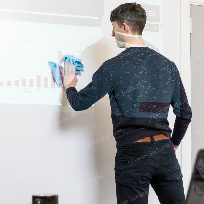 Man cleaning matte dry erase board paint wall surface with blue microfiber cloth.