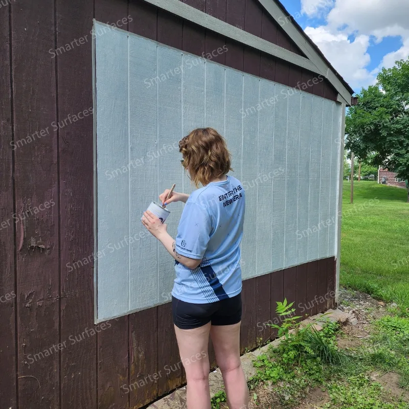 Person painting an exterior barn wall with outdoor projector screen paint