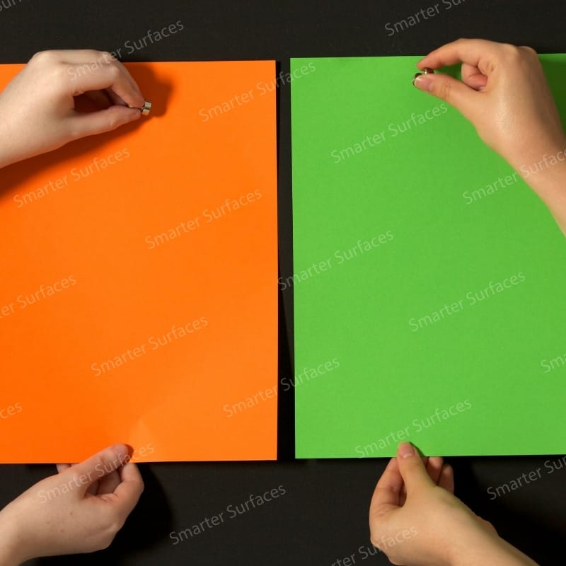 Hands demonstrating super magnetic paint functionality on orange and green painted strong magnetic wall surfaces