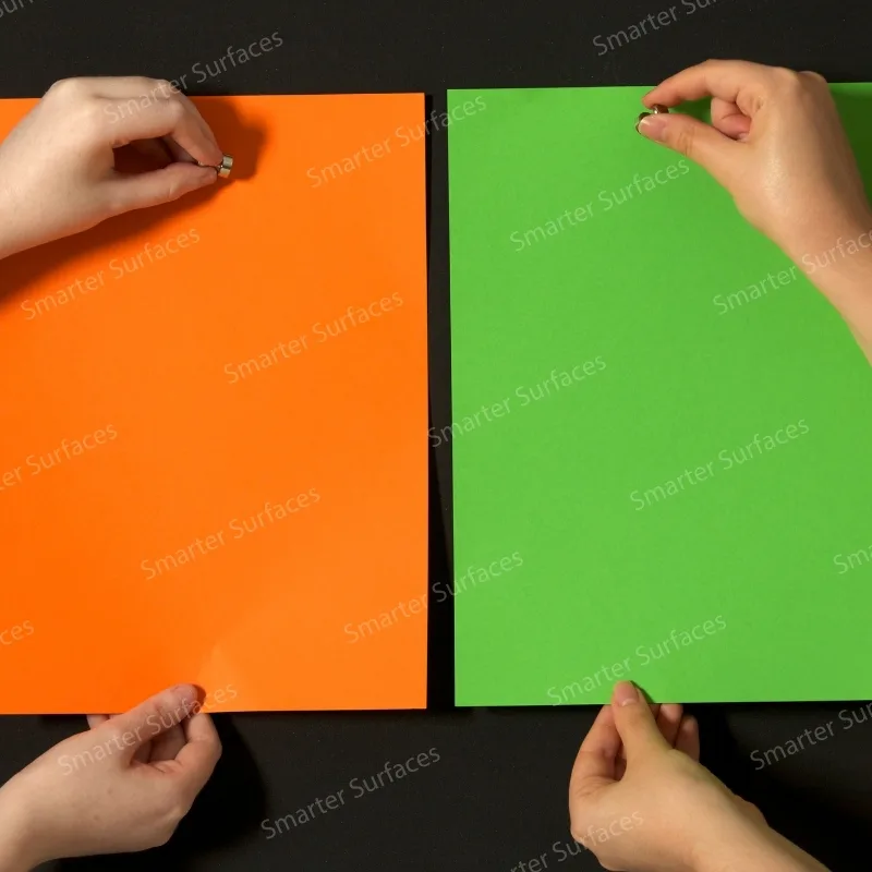 Hands demonstrating super magnetic paint functionality on orange and green painted strong magnetic wall surfaces