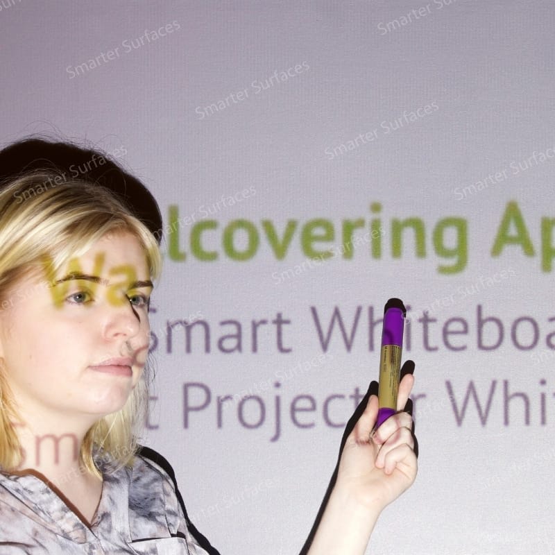A woman pointing at projected text displayed on a smooth wall coated with white projector screen paint.