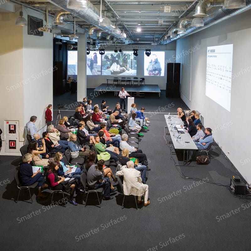 Audience in a large conference hall watching presentations projected clearly on walls coated with white projector screen paint.