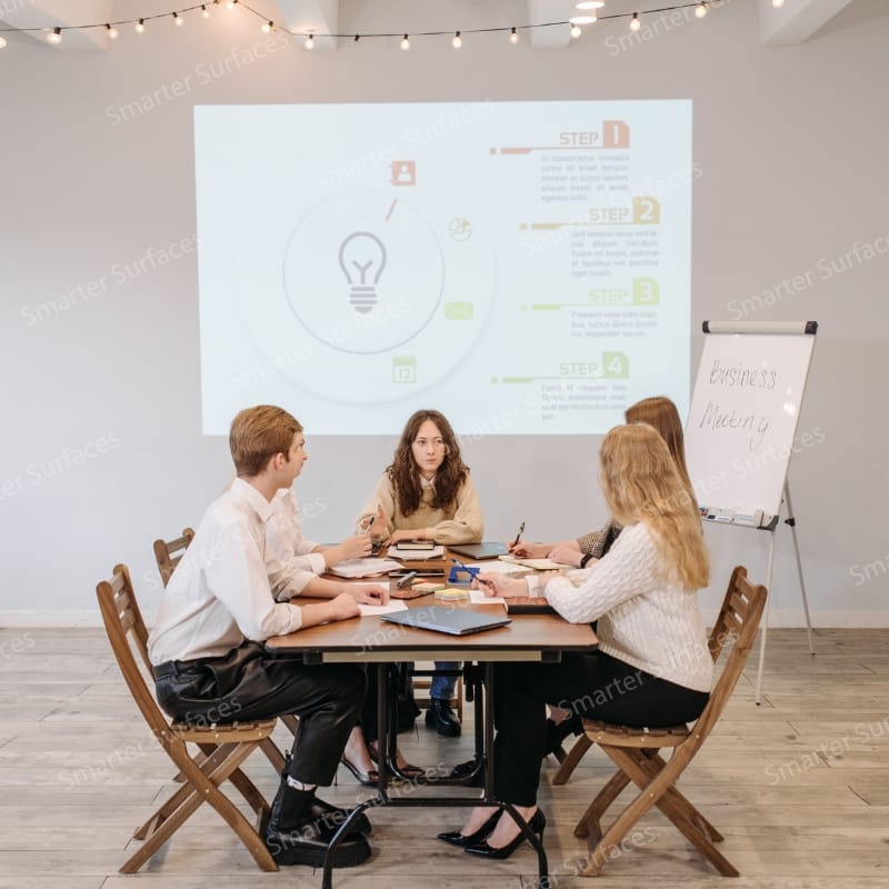Team having a business meeting with a bright, clear presentation projected onto a wall coated with white projector screen paint.