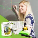 A woman is writing on a whiteboard-painted wall with a product kit in front of her.