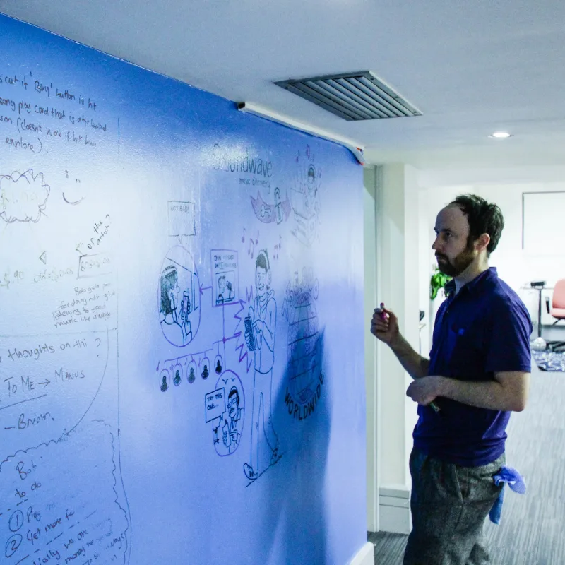 A man is writing on a large blue wall painted with dry erase whiteboard paint.