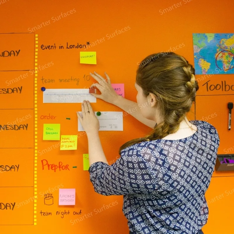 Woman organizing schedule on vibrant orange magnetic whiteboard wall.