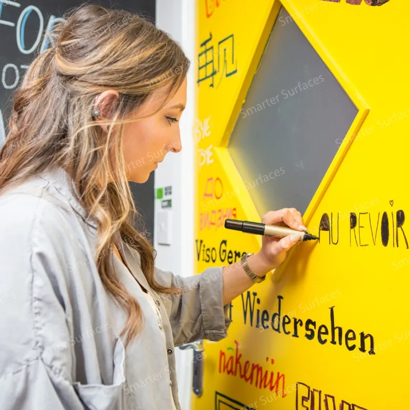 Woman writing on a yellow wall painted with dry erase whiteboard paint.