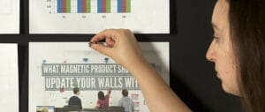 Person pinning printed charts and papers on a magnetic chalkboard wall.