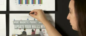 Person pinning printed charts and papers on a magnetic chalkboard wall.