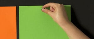 Hand pinning a green sheet of paper to a magnetic chalkboard wall.