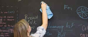 Child wipes a magnetic chalkboard wall clean with a cloth.