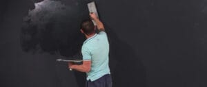 A man is applying magnetic chalkboard paint to a wall with a trowel