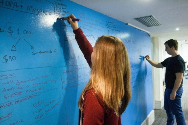 A woman and a man working together, writing on a whiteboard clear paint wall